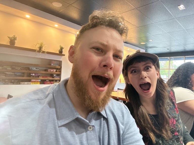 Two people making exaggerated excited expressions in an indoor setting with shelving visible in the background