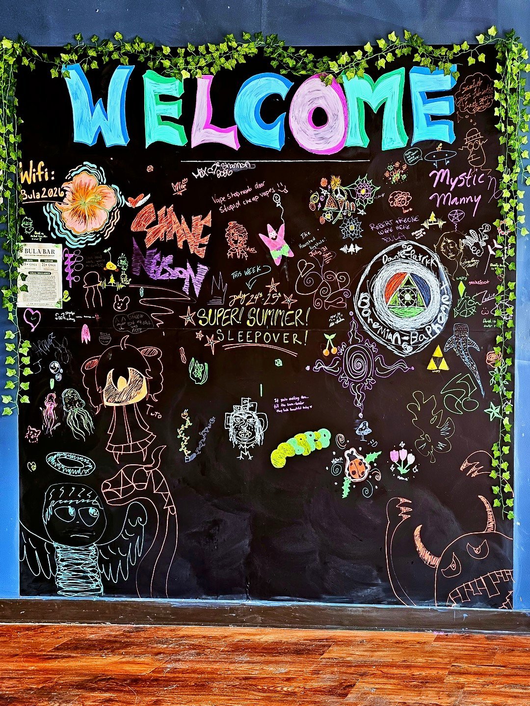 Colorful welcome bulletin board with chalk drawings, green vine border, and large blue and pink WELCOME text