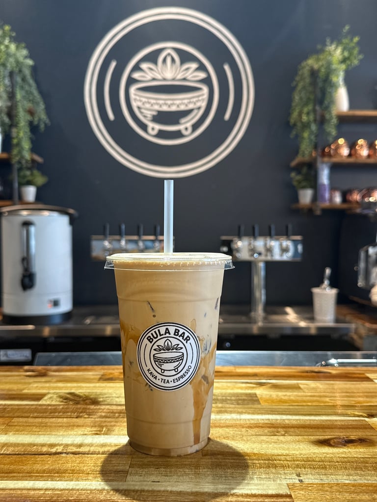 Iced milk tea drink in clear cup on wooden counter at Bula Bali cafe with neon logo sign on dark wall behind