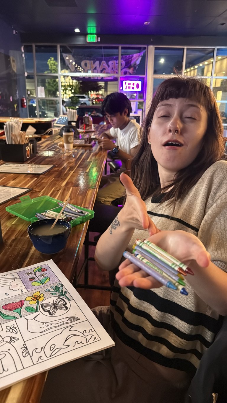 Woman holding markers at a table with coloring sheet in a dimly lit restaurant or bar with purple neon lighting