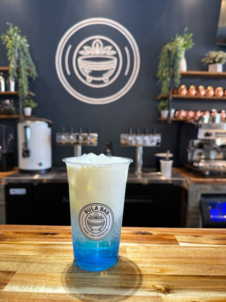 Blue and yellow layered iced drink in a clear cup on wooden counter in a modern cafe with neon smile logo on dark wall