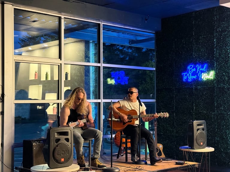 Two musicians performing acoustic music in a modern glass-walled studio with neon signage and blue lighting at night