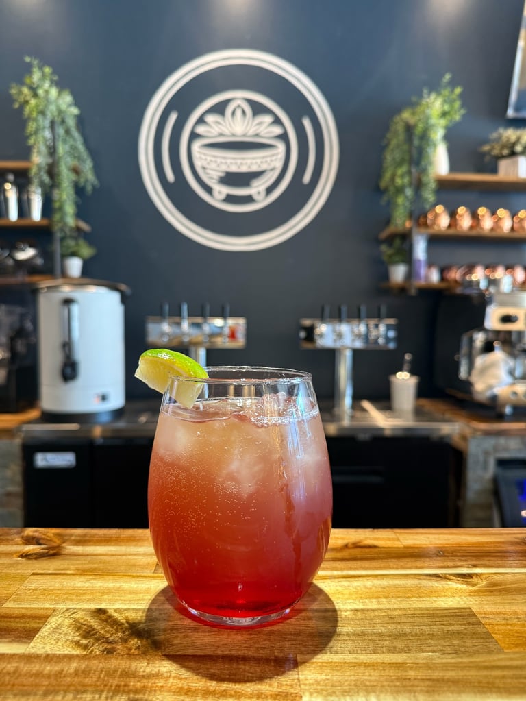 Red cocktail with lime garnish on wooden bar counter, modern restaurant interior with dark blue wall and circular logo sign