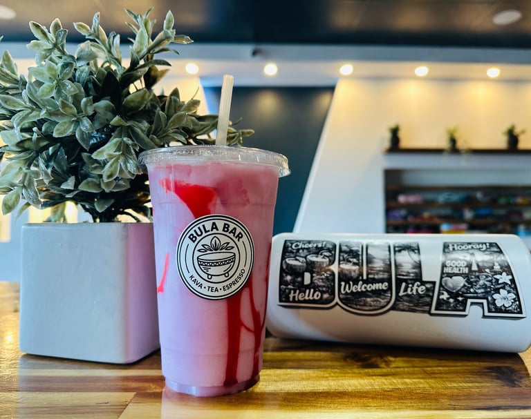 A pink beverage with a logo sits on a wooden counter next to a potted plant and decorative WELCOME sign in a modern cafe.