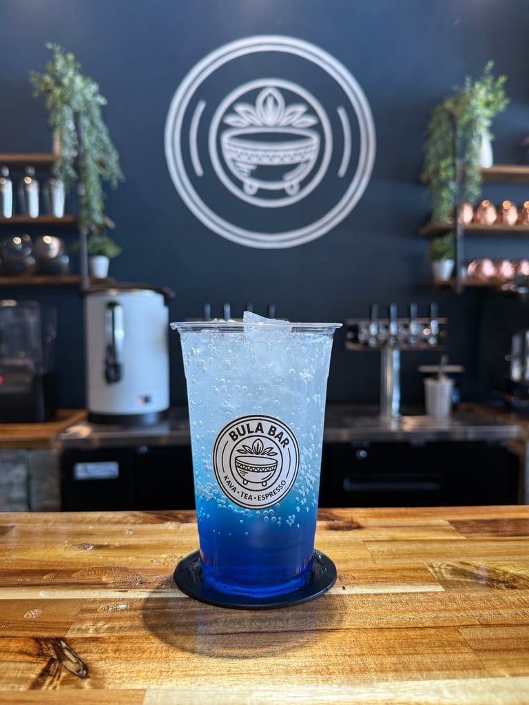Blue bubble tea drink on wooden counter at cafe with branded logo on wall and shelves with plants in background