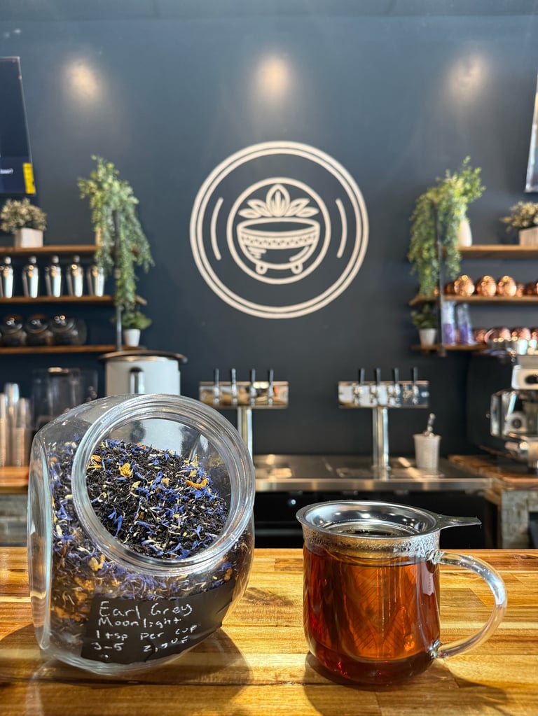 Tea shop counter with loose tea jar and brewed tea in glass cup, neon bowl logo on dark blue wall behind shelves with herbs and supplies