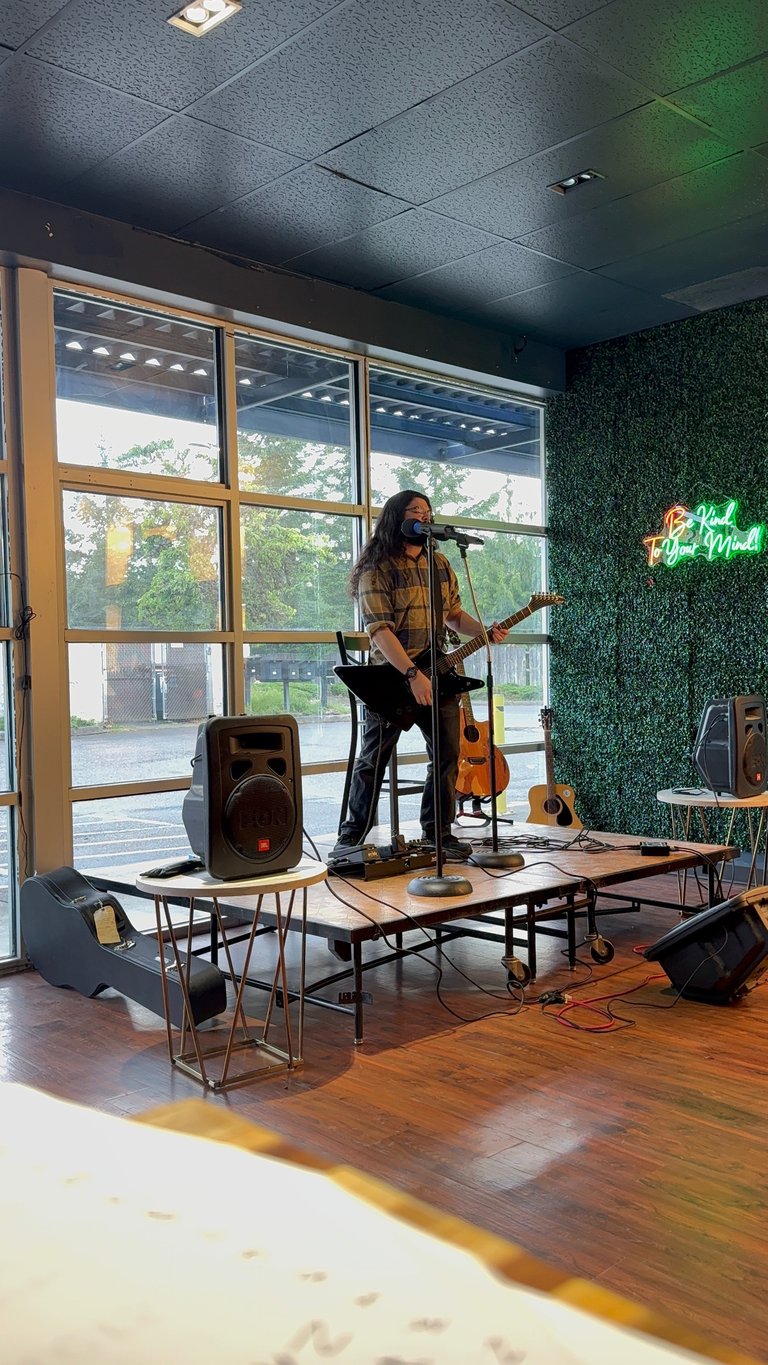 Musician performing on stage with guitar and microphone in modern venue with large windows and green wall decor