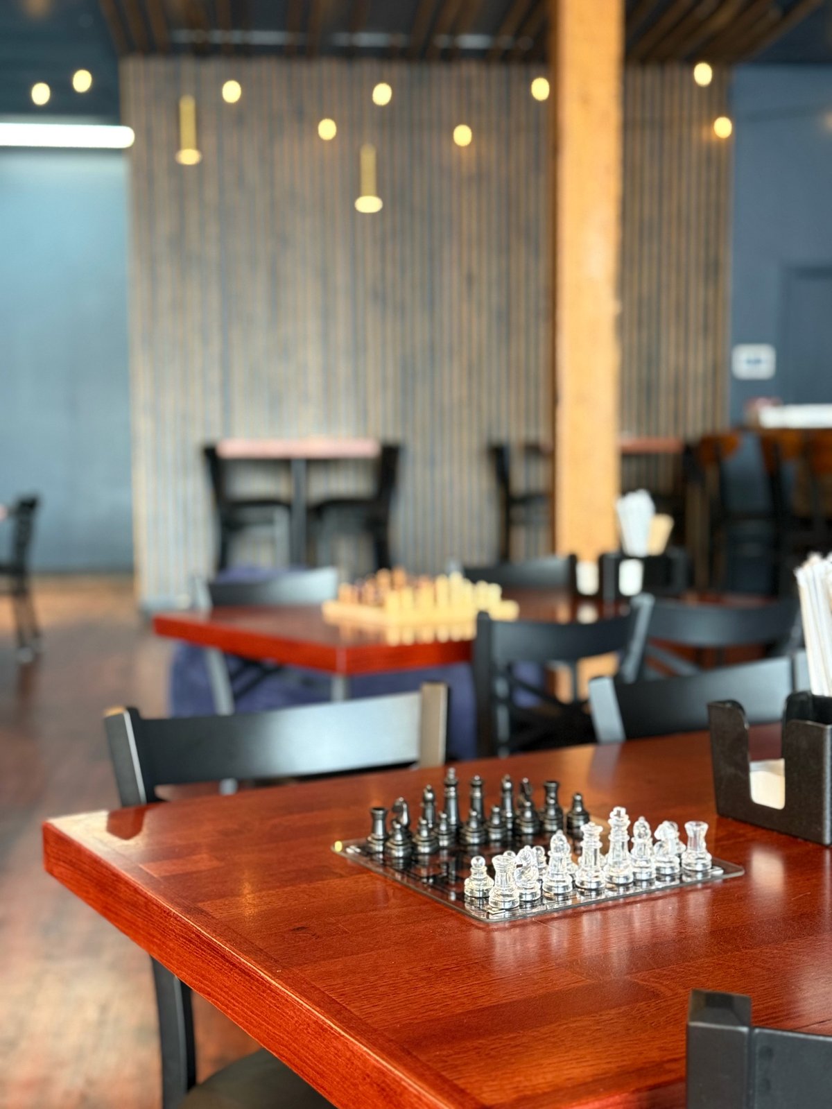 Chess set on wooden table in modern lounge with pendant lights and floor-to-ceiling windows
